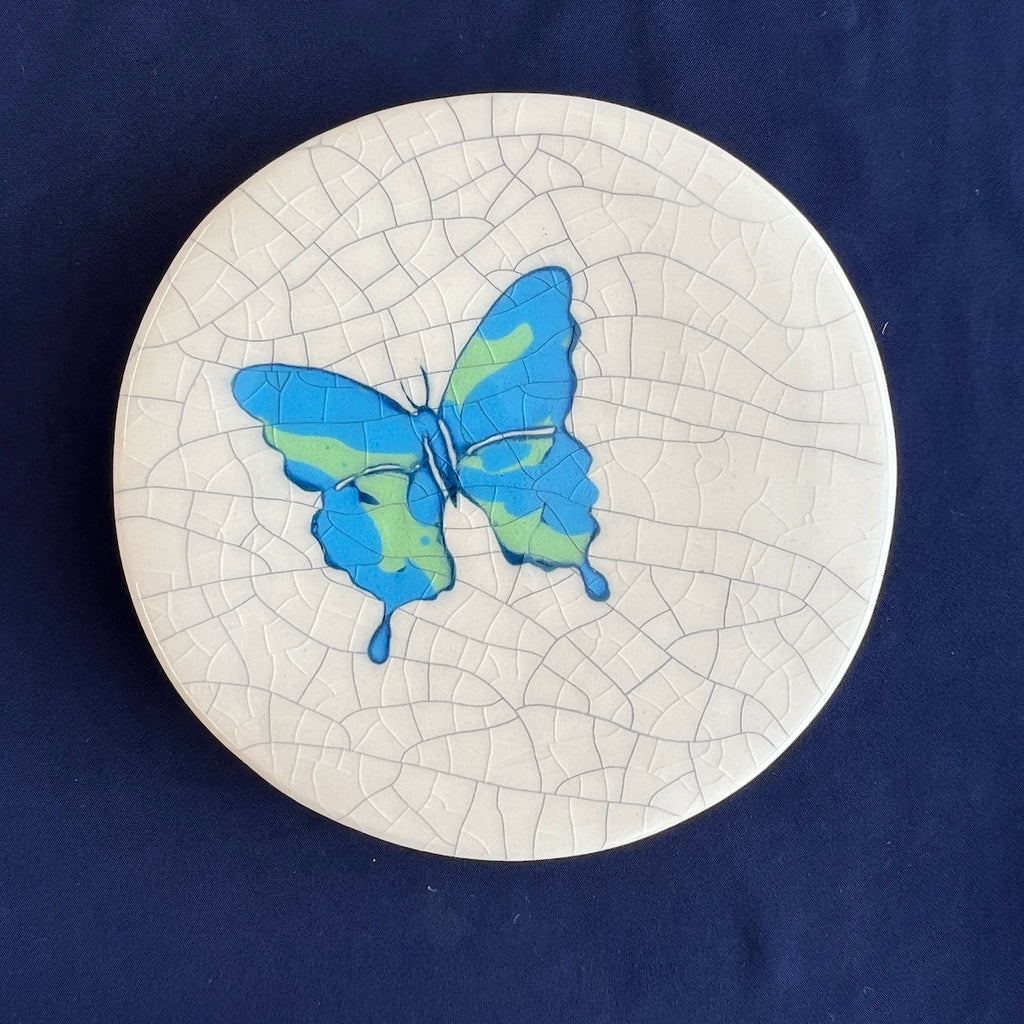 Round ceramic coaster with a blue butterfly design on a crackle glaze background