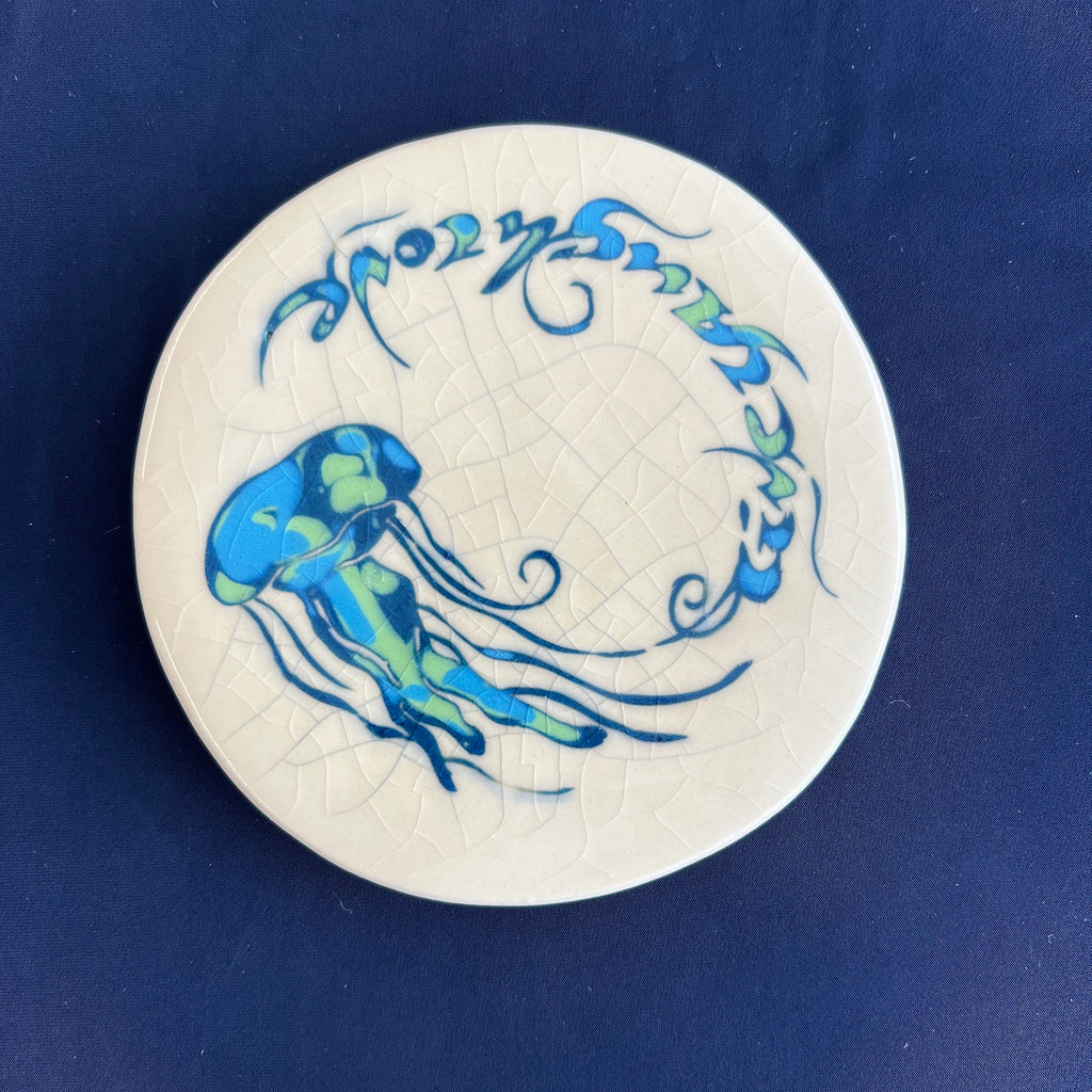 Round white coaster with blue jellyfish design on a crackle glaze background