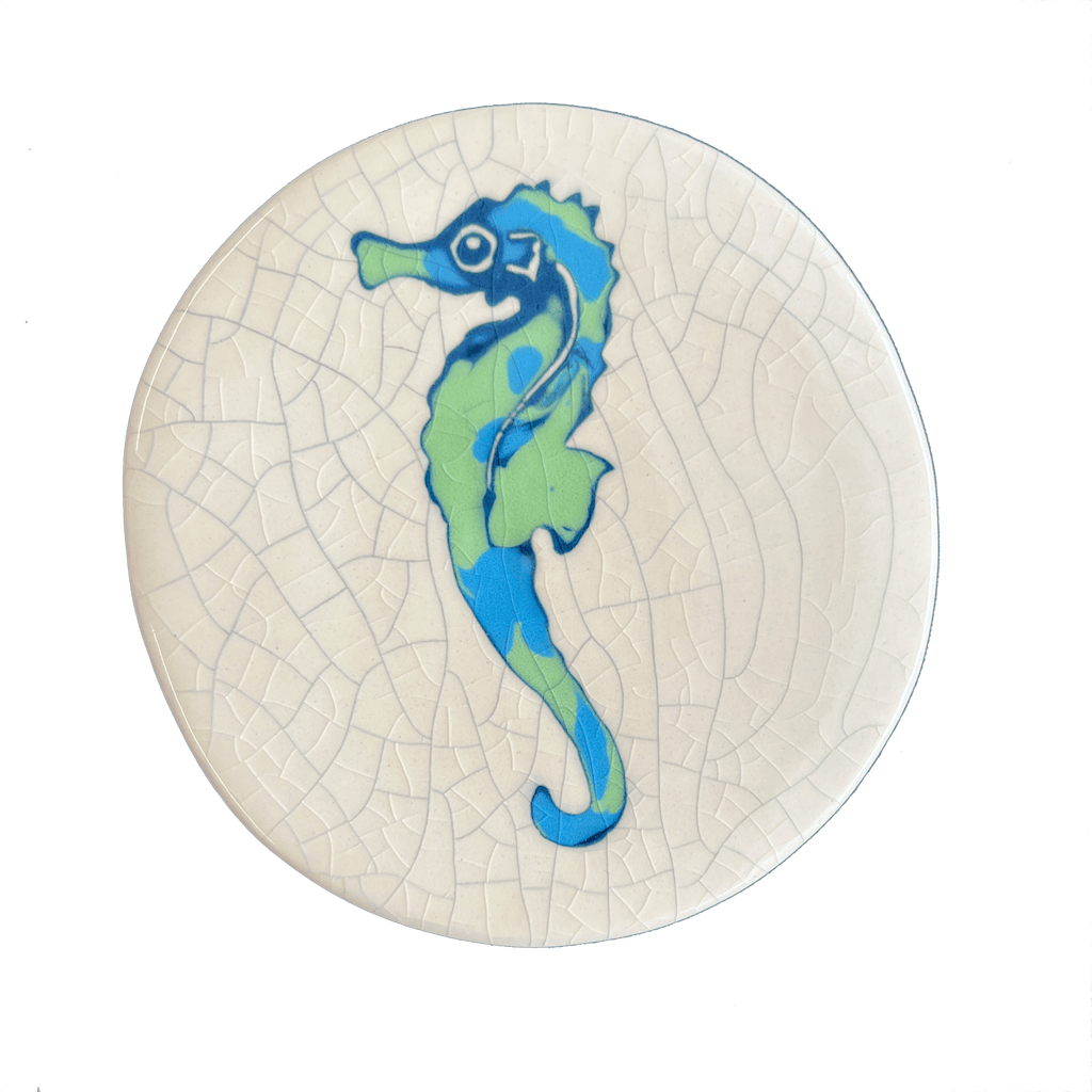 Round ceramic coaster with a blue and green seahorse design on a textured white background